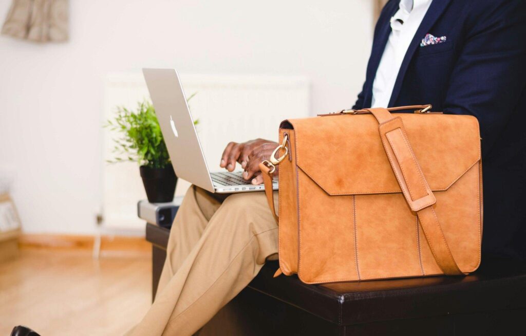 A stylish businessman working on a laptop indoor with a leather briefcase.